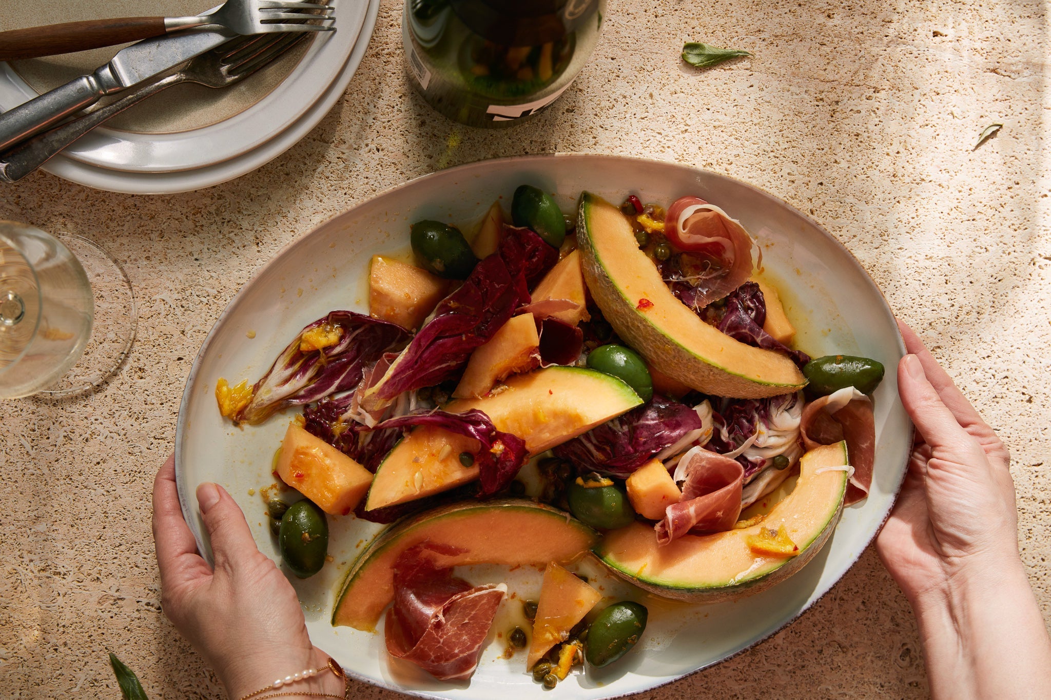 Plated dish of melon, prosciutto, and radicchio held by a person on a textured surface.